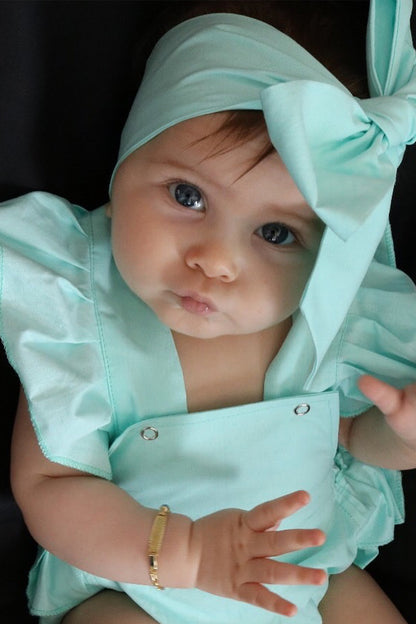 Baby mit Haarband und Salopette in türkis